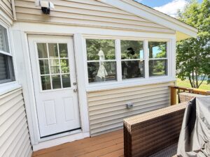 Exterior of a sunroom with a white paneled door featuring a nine-pane glass insert next to a white-framed triple window, on a wood deck